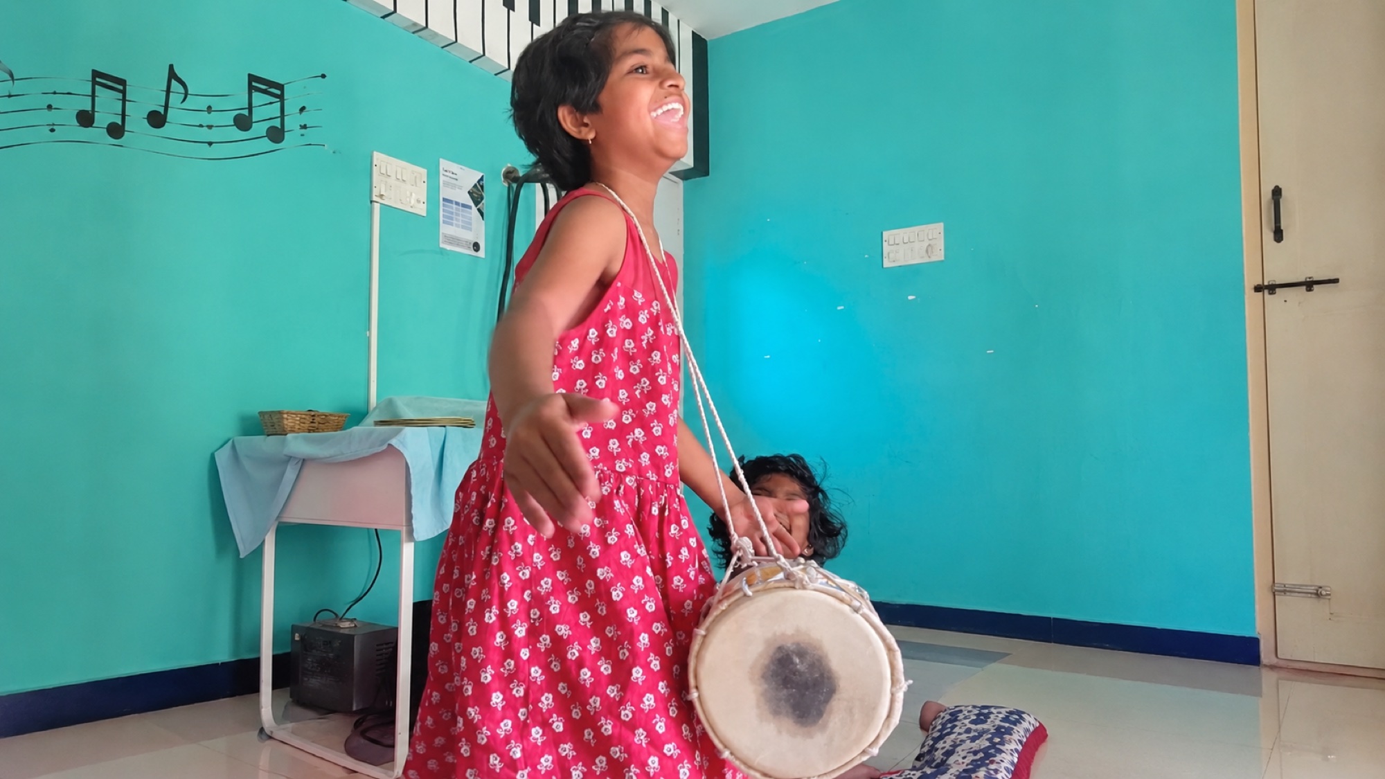 Sing for Hope student playing a small drum with music notes on the wall
